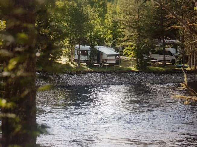 Ett naturskönt område vid Ammeråns Fiskecamp med en porlande ström omgiven av tät skog och gröna växter längs flodbanken.