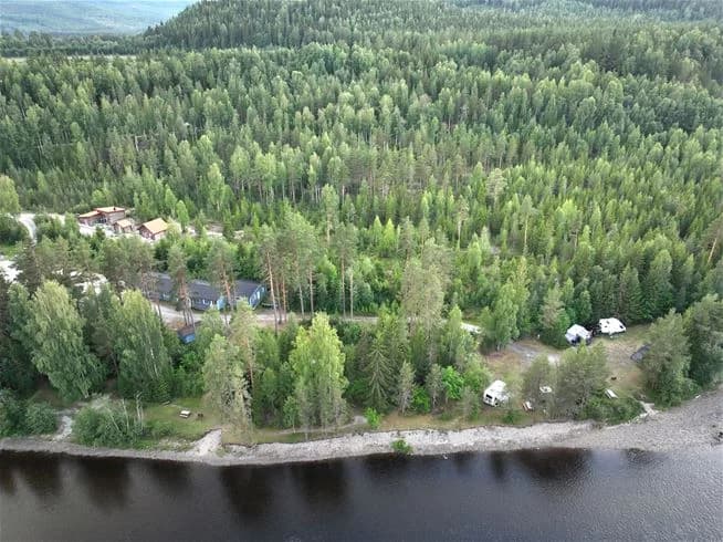 En liten stuga omgiven av tät skog med höga granar i ett naturskönt område vid Ammeråns fiskecamp.