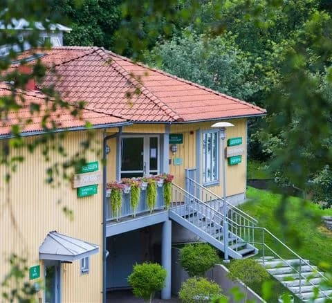 En mysig stuga med en veranda och trappa omgiven av ett staket, perfekt belägen i en grönskande trädgård på Lisebergsbyn.