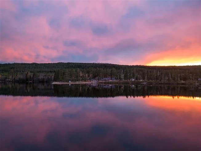En stilla sjö vid skymningen vid Kojbyns camping, med en klar blå himmel som möter horisonten i fjärran.
