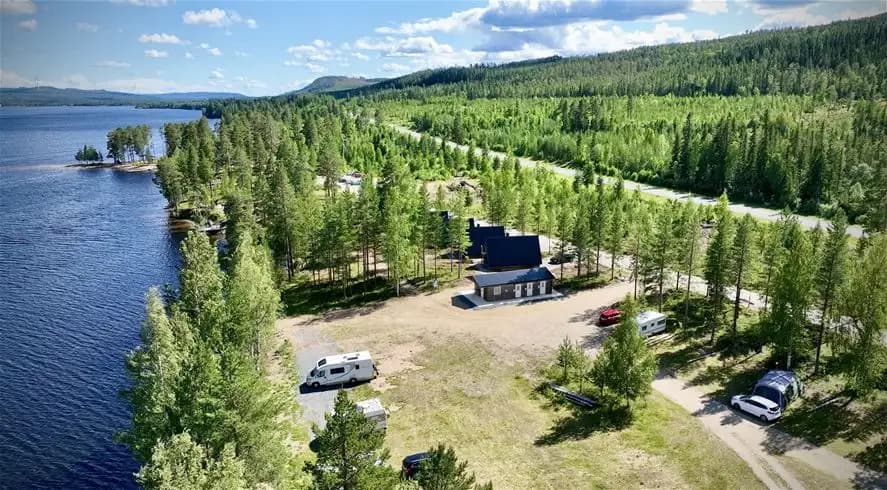 En fridfull sjö i skogsmiljö vid Kojbyns camping, omgiven av täta barrträd och lövträd.