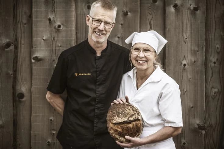 En leende kock iklädd kockuniform och förkläde står vid Kojbyns Camping, redo att laga mat.