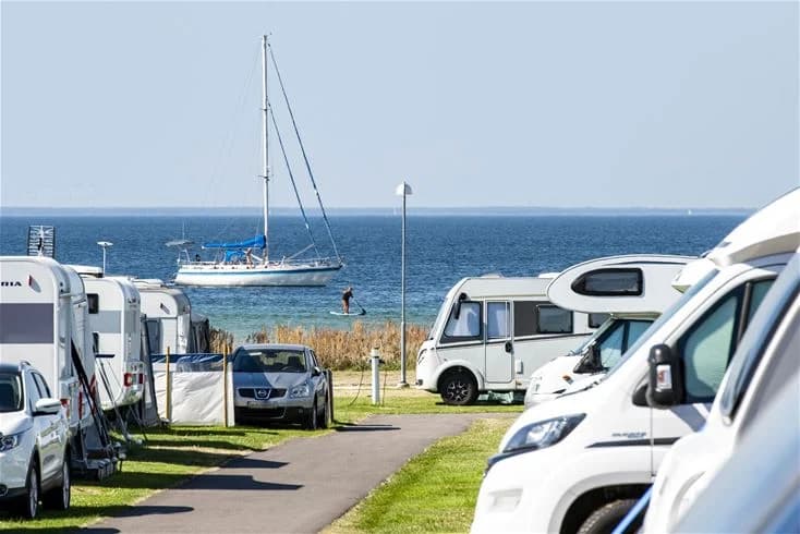 Bild av Gröndals camping & stugor som visar en husvagn parkerad nära havet med utsikt över stranden. En bil står bredvid husvagnen och ett lugnt hav syns i bakgrunden.