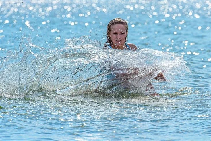 En grupp glada människor har roligt och njuter av sommaren på Gröndals camping & stugor, omgivna av vattenaktiviteter och vågor som skapar en livlig och avslappnad semesterstämning.