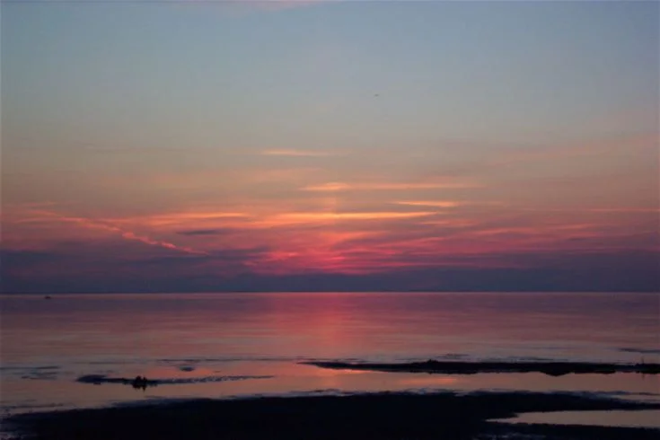 En vacker solnedgång över horisonten vid Gröndals Camping & Stugor med en himmel i blått och orange, samt vattenreflektioner under en molnfri skymning.