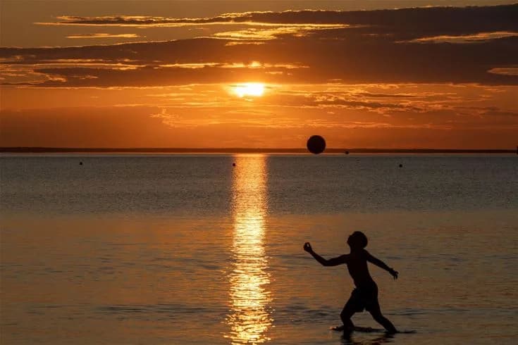 En solnedgång vid Gröndals Camping & Stugor, där himlen är färgad i orange och efterglöd, med havet som breder ut sig framför stranden.