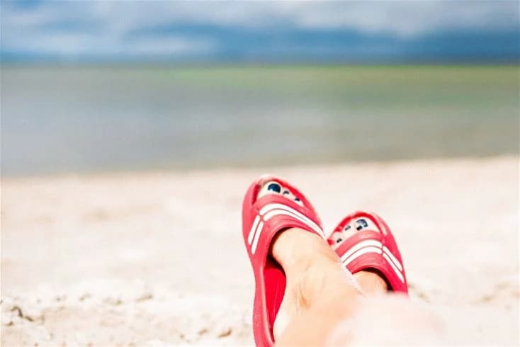 En grupp människor som går barfota i sanden nära vattnet på Gröndals camping & stugor, med havet synligt i bakgrunden.