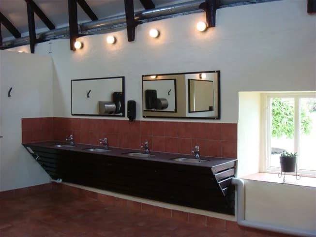 Ett modernt badrum på Gröndals Camping & Stugor med trägolv, vitkaklade väggar, en stilren handfat med blandare och ett ljust tak.