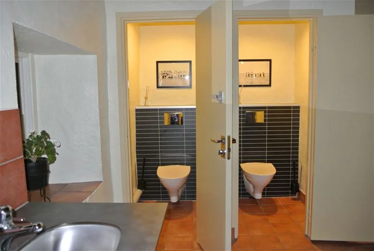 En stilren och välskött badrumsmiljö med kaklade väggar och golv. Det finns en modern handfat med blandare och ett spegelskåp ovanför, vilket skapar en fräsch och funktionell atmosfär.