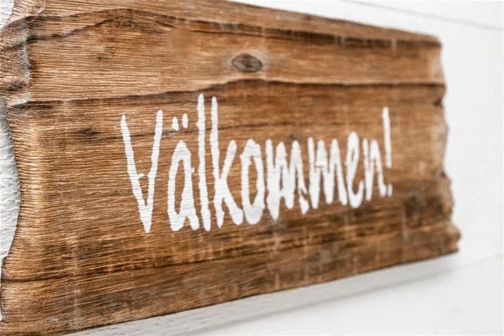 Bild av en träskylt vid Gröndals Camping & Stugor, gjord av bearbetat trä med tydlig text. Skylten är placerad mot en naturlig bakgrund av träd och campingområdet, vilket ger en välkomnande känsla.