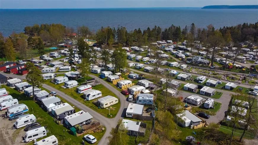 Flygbild över Ursand Resort & Camping, med en kustlinje som möter ett blått vatten. Stranden syns längs kusten och platsen framstår som en populär turistattraktion för rekreation.