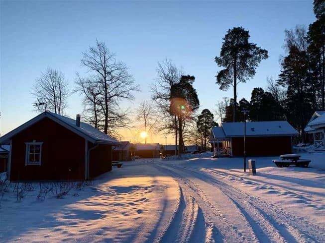En snötäckt stuga omgiven av grenar med snö på, belägen i ett vinterlandskap vid Skantzö Bad & Camping.