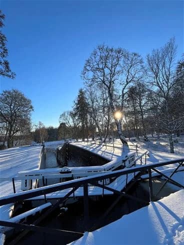 En snötäckt träbro omgiven av trädgrenar, sett på Skantzö bad & camping under vintern.