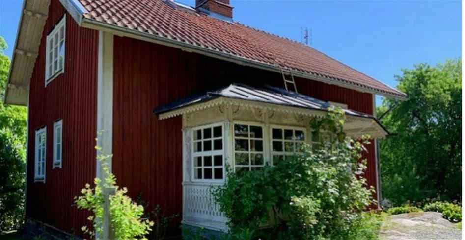 Alt-text: En trästuga med sadeltak vid Skantzö Bad & Camping, omgiven av buskar och grönska.