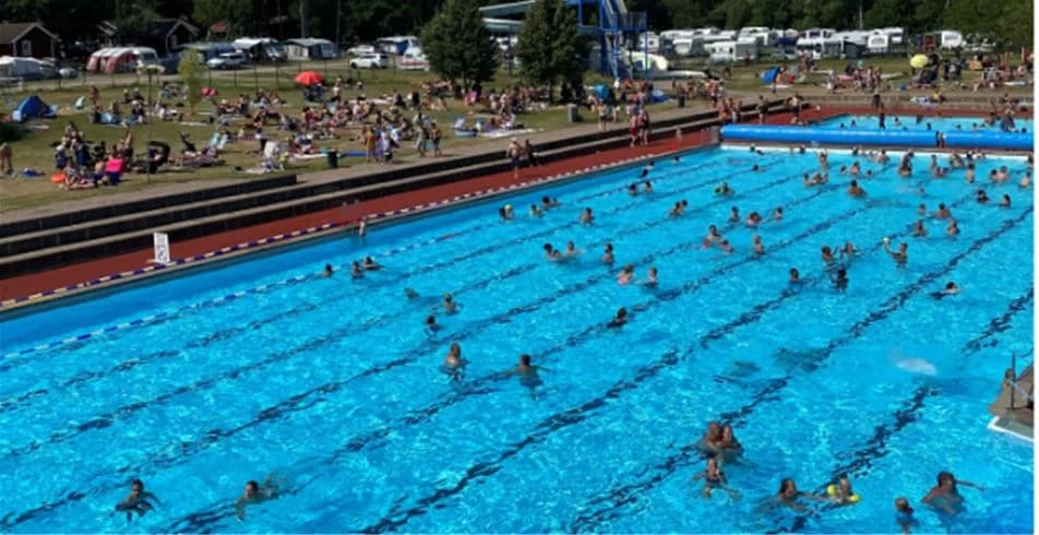 En grupp människor har roligt på en campingplats med pool och sportaktiviteter, omgiven av grönska, på Skantzö Bad & Camping.