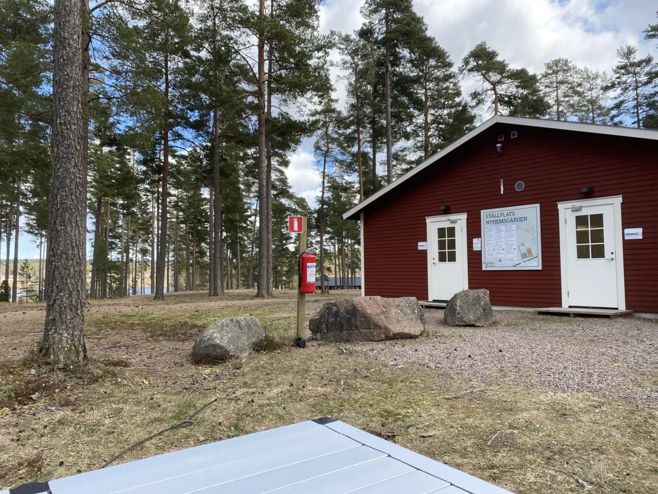 En charmig stuga på landsbygden med träd och en liten gård framför. En enkel uppfart leder fram till dörren, och en mindre byggnad eller skjul syns i bakgrunden.