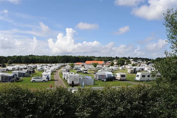 En husbil parkerad på en campingplats vid Grebbestadfjorden, med flera husvagnar och bilar synliga i bakgrunden på parkeringsplatsen.
