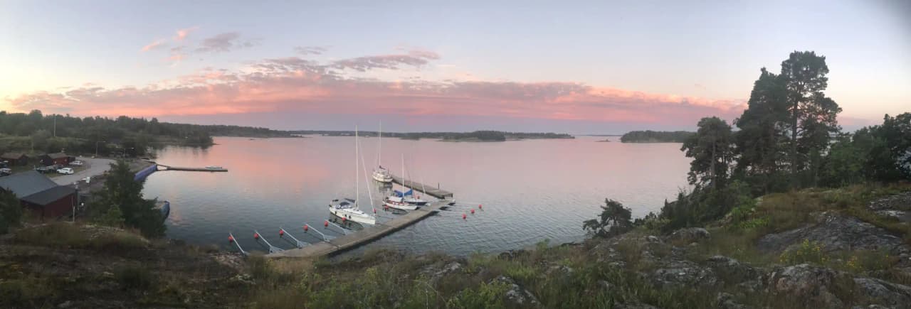 En segelbåt ligger förtöjd vid en brygga vid Tyrislöt Camping, omgiven av en stilla vattenväg och grönskande kustlinje.