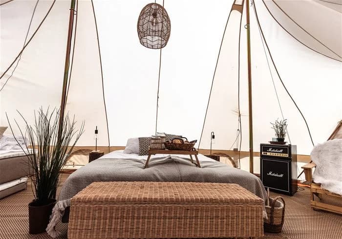 En campingplats vid Grebbestadfjorden med tält uppsatta på en grön gräsmatta, omgiven av träd. Ett rep används som del av tältuppsättningen.