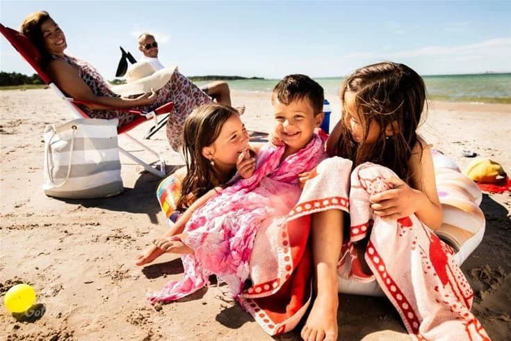 En solig sommardag på Kneippbyn Resort Visby med folk som njuter av semestern på stranden, leker och kopplar av i naturen med leenden på läpparna.