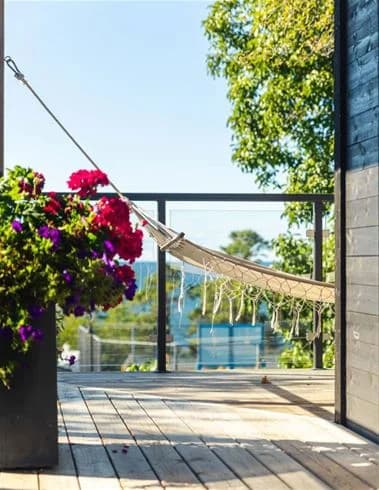 Beskrivning av bilden: Ett uteområde på Kneippbyn Resort Visby med trädäck och trämöbler. Det finns blomkrukor som skapar en inbjudande atmosfär. Skuggor från omkringliggande objekt ger ett behagligt ljus över området.