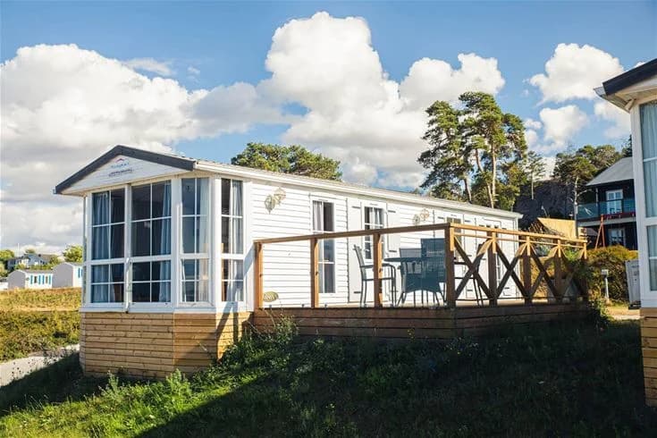 Alt-text: En trästuga med veranda på Kneippbyn Resort Visby. Stugan har träpanel och är omgiven av trädäck, perfekt för en avkopplande vistelse.