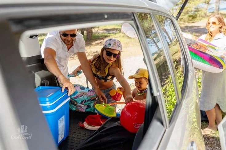 En familj packar bilen för en roadtrip vid Kneippbyn Resort Visby, glada ansikten och en öppen bagagelucka med semesterpackning.