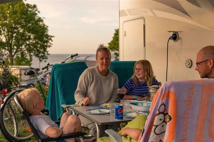 En glad familj njuter av semestern vid Kneippbyn Resort Visby, sittandes bekvämt på utemöbler och upplever fritid och rekreation i en avslappnad miljö.