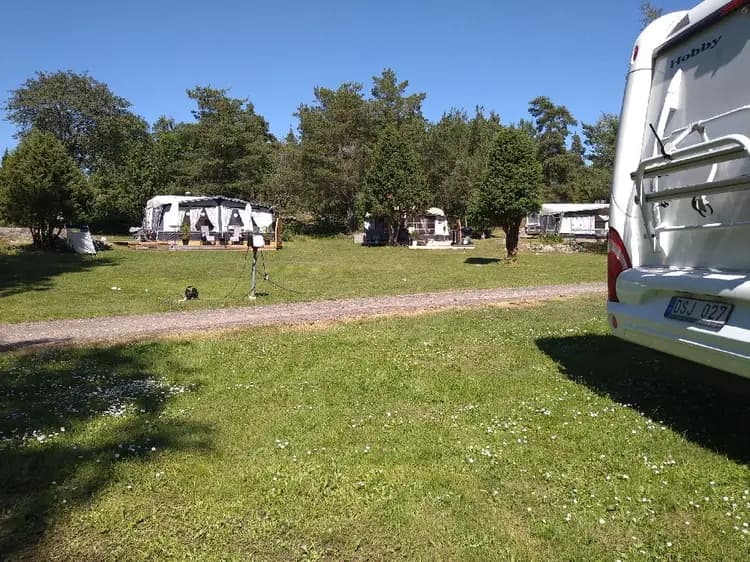 En bild som visar gräsöbadens familjecamping med flera husbilar och husvagnar parkerade på gräsmattan. Besökare njuter av campingupplevelsen i en naturskön miljö.