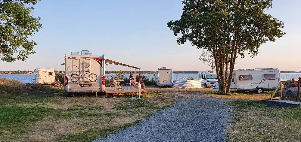 En kustnära campingplats vid havet där flera husvagnar står parkerade, med en sandstrand och vik i bakgrunden.
