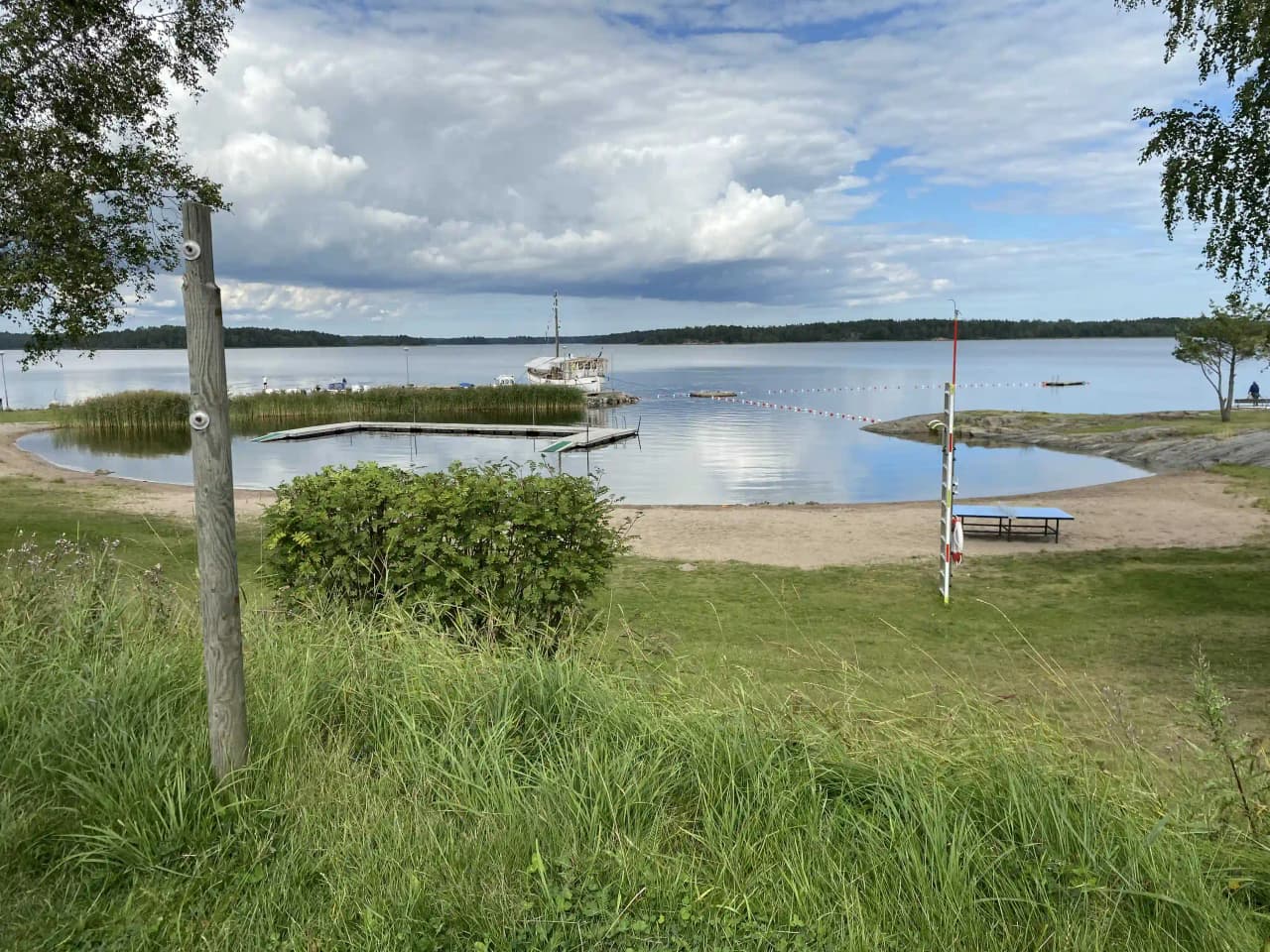 En naturskön vy över vatten vid Hargshamns camping, med båtar förtöjda längs en kust och omges av lummiga skogspartier.