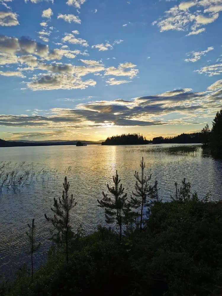 Vy över Rätans camping med en klarblå himmel, spegeltjärn och omgivande natur.