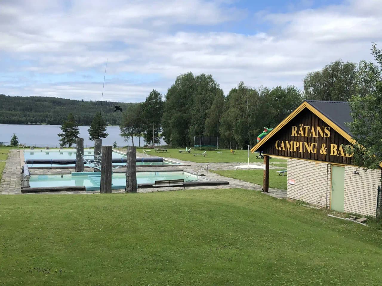 Bild av Rätans camping som visar en grönskande anläggning med pool, välskötta gräsmattor och omgivande träd, vilket skapar en fridfull och inbjudande atmosfär för besökare.