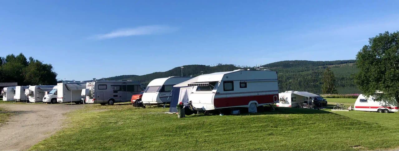 En husvagn och flera campingfordon parkerade på Rätans camping under en klar himmel med moln.
