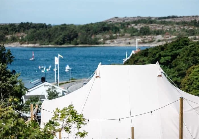 En campingplats i Grebbestadfjorden med ett tält under en presenning, omgiven av frodig natur.