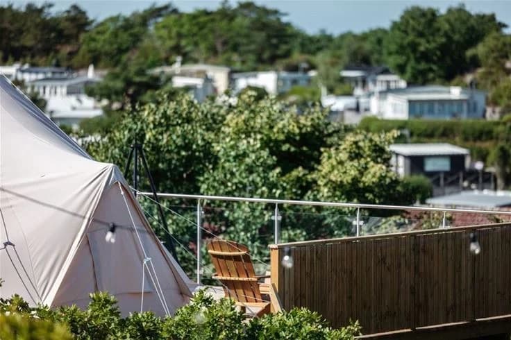 Bild på en campingplats vid Grebbestadfjorden, med flera tält och utomhusmöbler under skuggande parasoller och presenningar, vilket skapar en inbjudande atmosfär för camping.