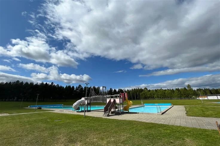 En livlig campingplats med besökare som njuter av aktiviteter vid en pool. Parker och fritidsområden syns i bakgrunden.