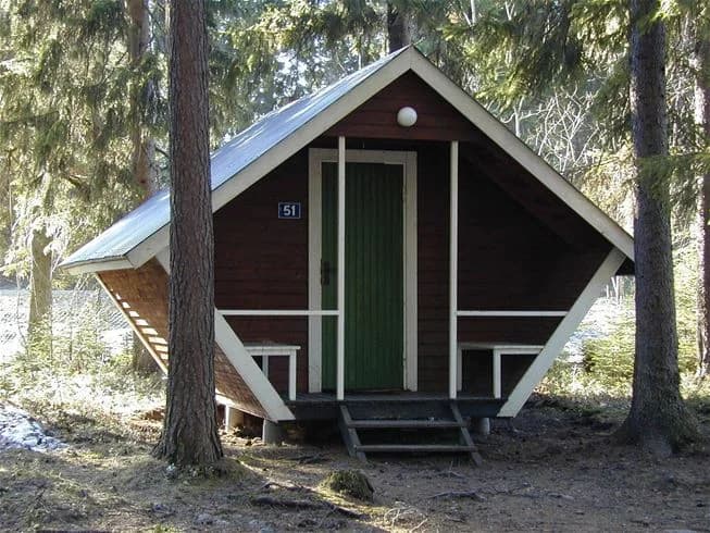 En timmerstuga omgiven av tät skog i Strömsunds camping, med träpaneler och en rustik charm.