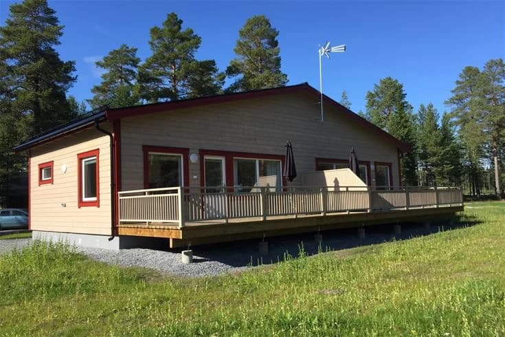 En mobil hemvagn med träsiding står parkerad på en grönskande camping. Trästommen är av hårdträ och har en djup träbets som ger en varm känsla i det naturnära omgivningen.