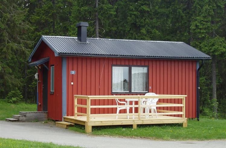 En timmerstuga på Strömsunds camping omgiven av grönska och träd. Byggnaden är gjord av bruna träplankor och har ett rustikt utseende.