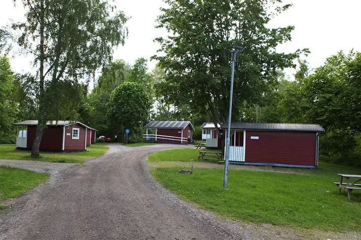 En grön campingplats med gräs och träd omger mysiga stugor vid Djulö Camping.