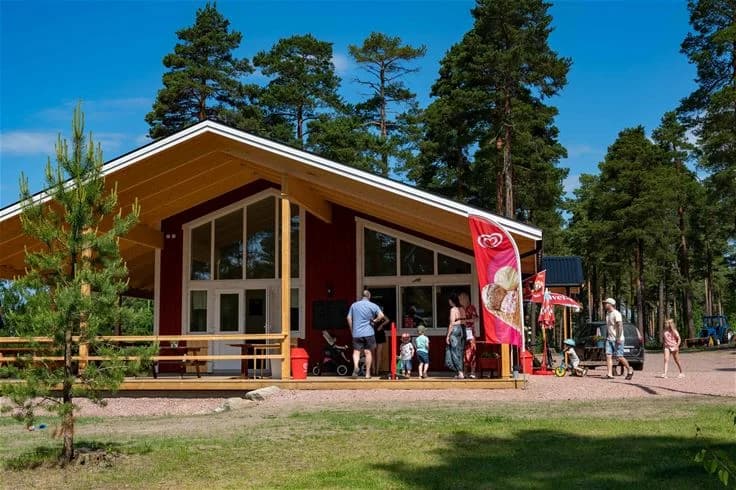 En mysig stuga omgiven av gröna träd och gräsyta, med skuggiga områden för rekreation på norra Dellen familjecamping.