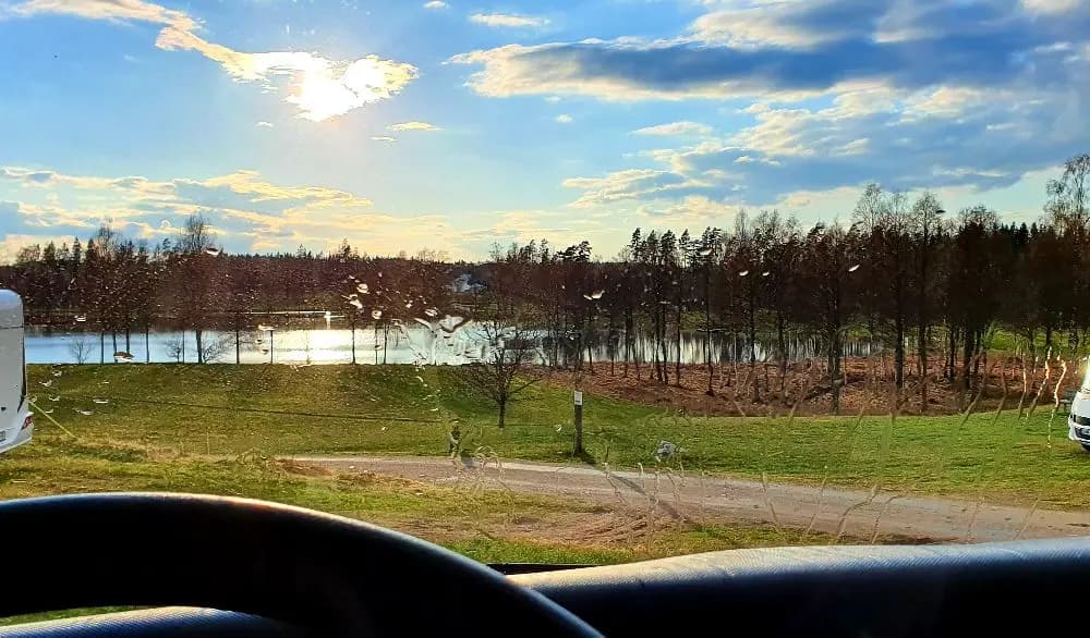 Alt-text: "Utsikt genom en bilruta på en biltur med sikte mot himlen, moln och vägen framför, på väg till Påarps gård."