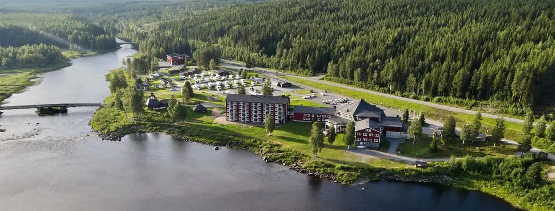 En naturskön vy över en flodkanal vid Storforsens camping, omgiven av frodiga flodbanker och skog, som skapar en lugn och avkopplande miljö för besökare.