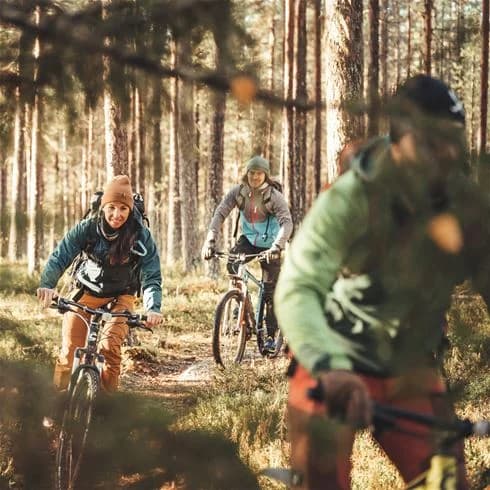 En person cyklar med mountainbike i naturskön miljö vid Storforsens camping. Cyklens däck och ram är tydliga detaljer, och cyklisten bär hjälm.
