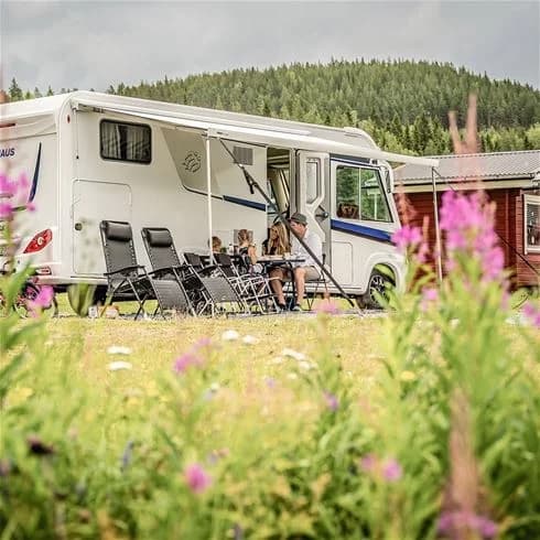 En campingplats med flera husbilar och husvagnar parkerade i ett naturskönt område, några cyklar syns i närheten av fordonen.
