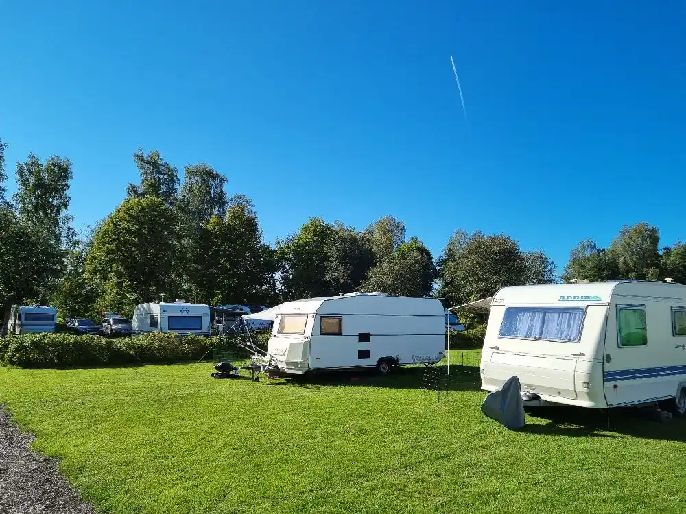 En campingplats med flera husvagnar och en större husbil parkerade i ett grönskande område.