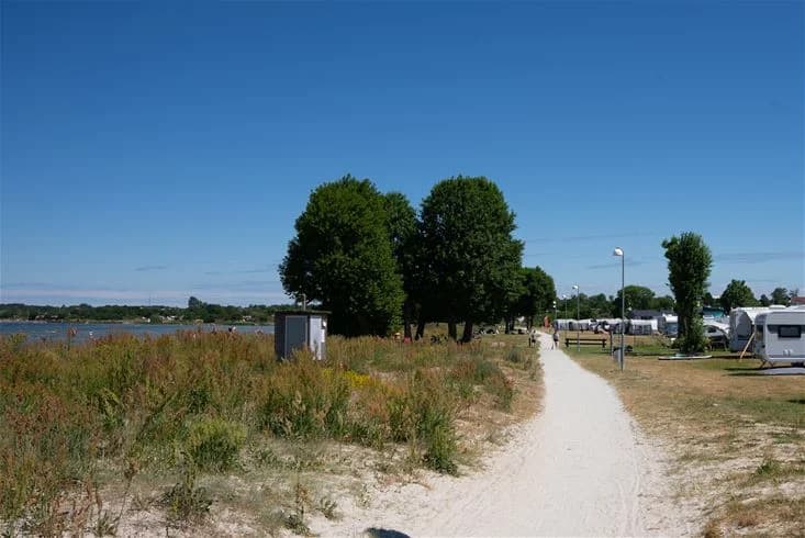 En somrig strand vid en kustlinje med havsutsikt, där människor njuter av rekreation vid Grönhag Camping.
