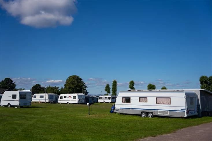 En campingplats med husvagnar och husbilar uppställda på en grön gräsmatta under en himmel med vita moln.
