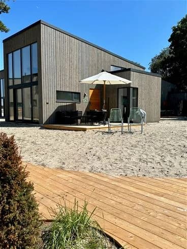 Alt-text: En träbyggnad med sidoklädsel av plankor på Köpingbaden Camping, omgiven av natur och strategiskt designad för att smälta in i den omgivande miljön.